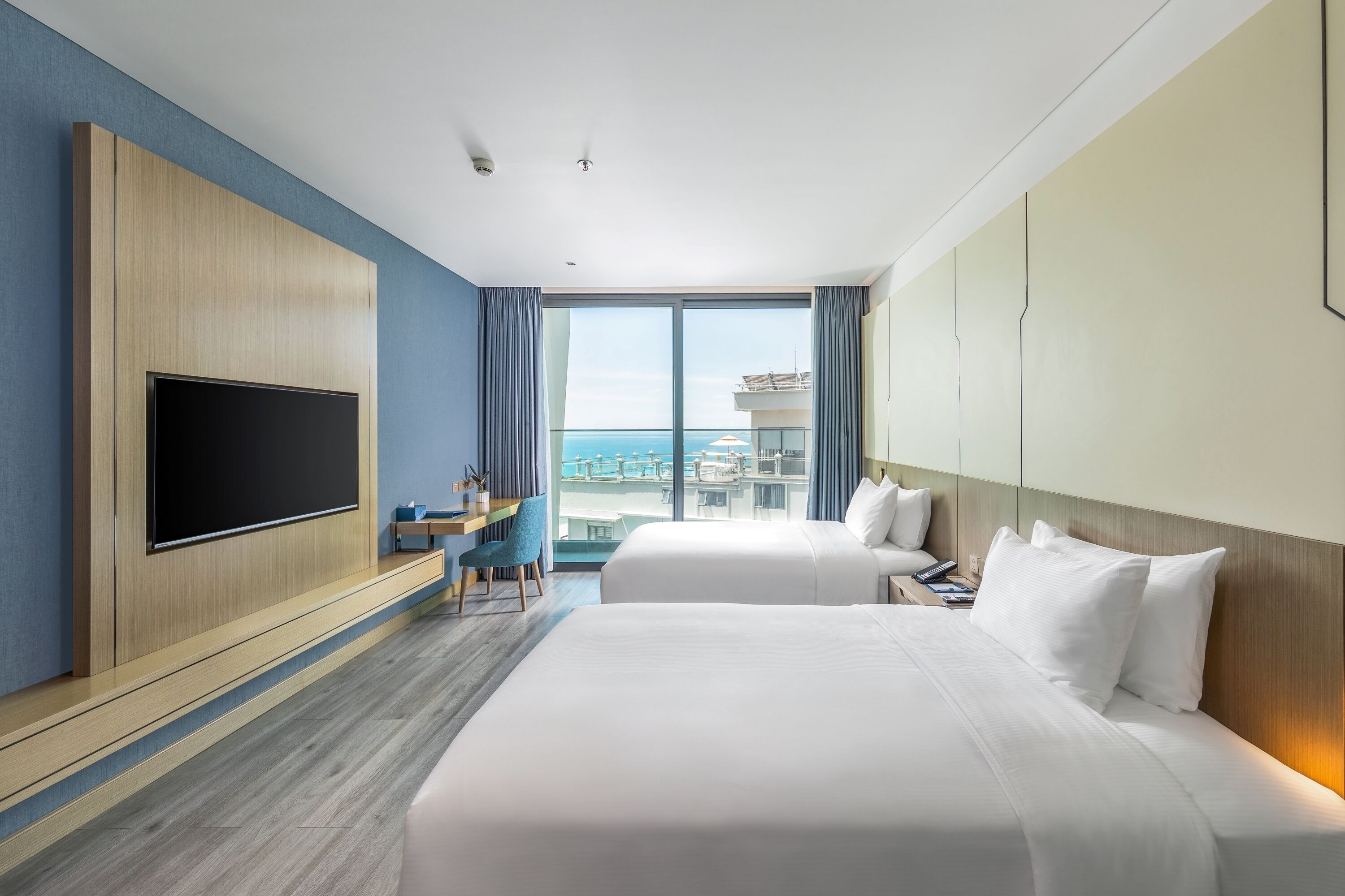 A hotel room with a large flat-screen TV, two beds, a desk, and a view of the city.