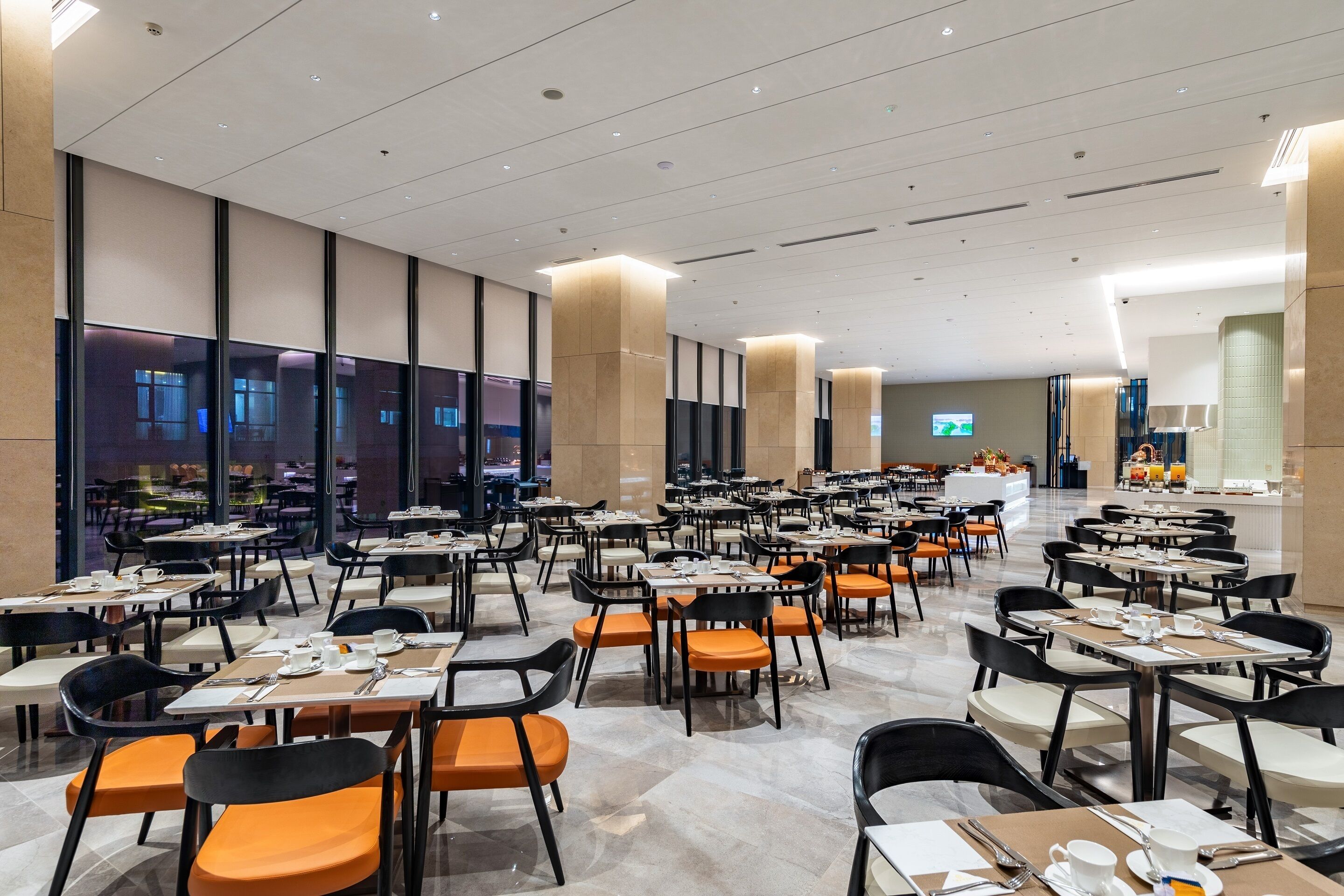 A spacious dining area with multiple tables and chairs, large windows, and a modern interior design.