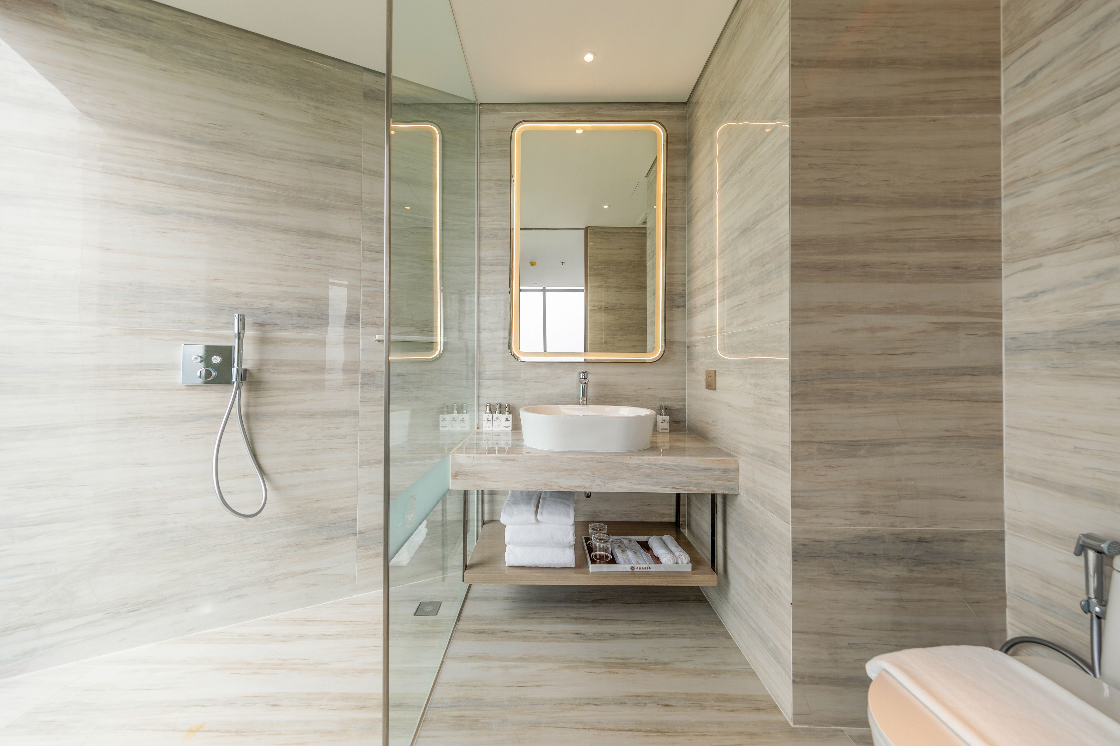 A modern bathroom with a glass-enclosed shower, a marble vanity, and a large mirror with illuminated edges.