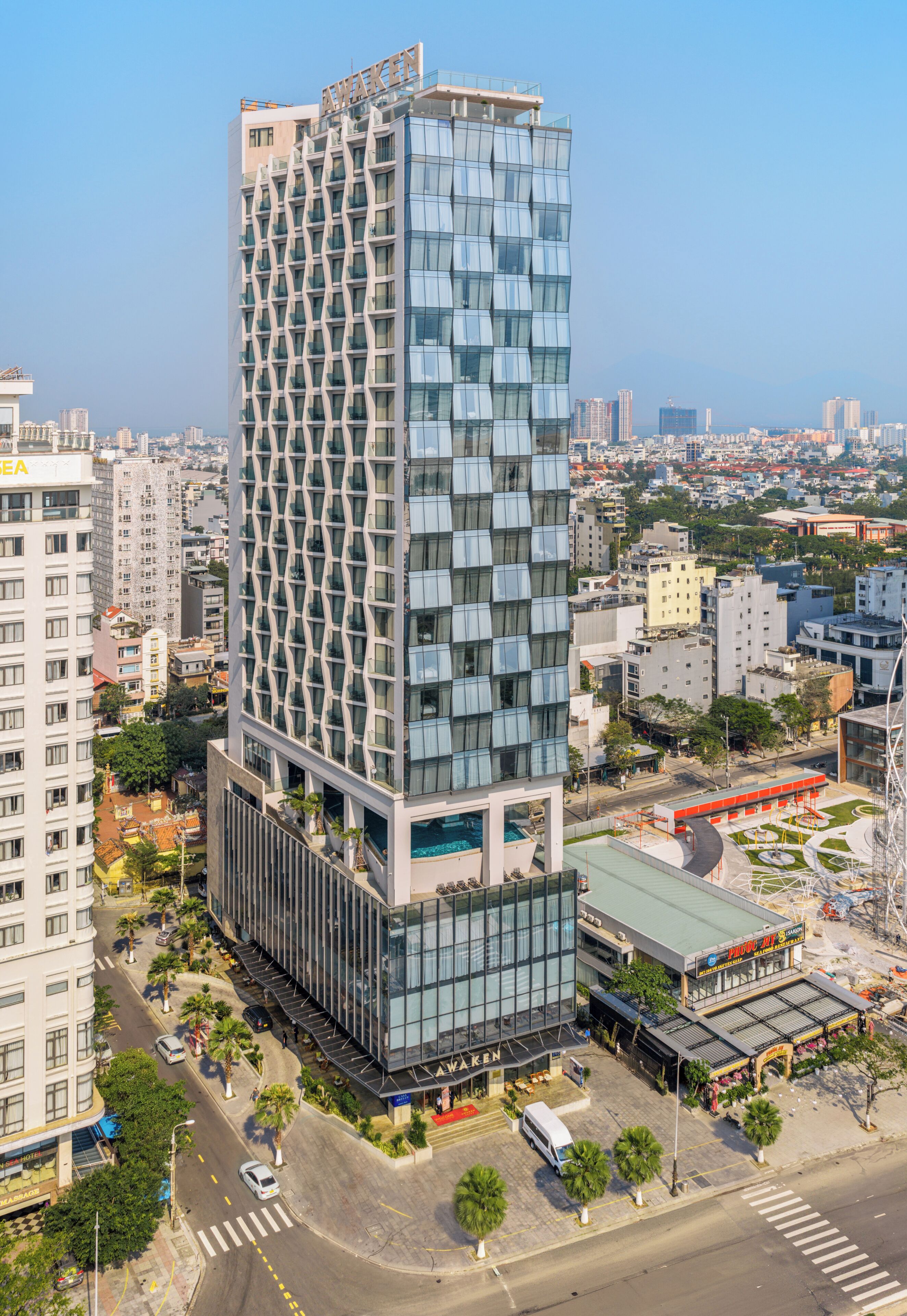 A high-rise building with a modern glass facade, surrounded by other buildings and a clear sky.