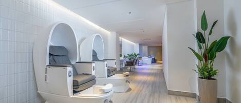 A modern spa room with a massage chair, a small seating area, and a potted plant.