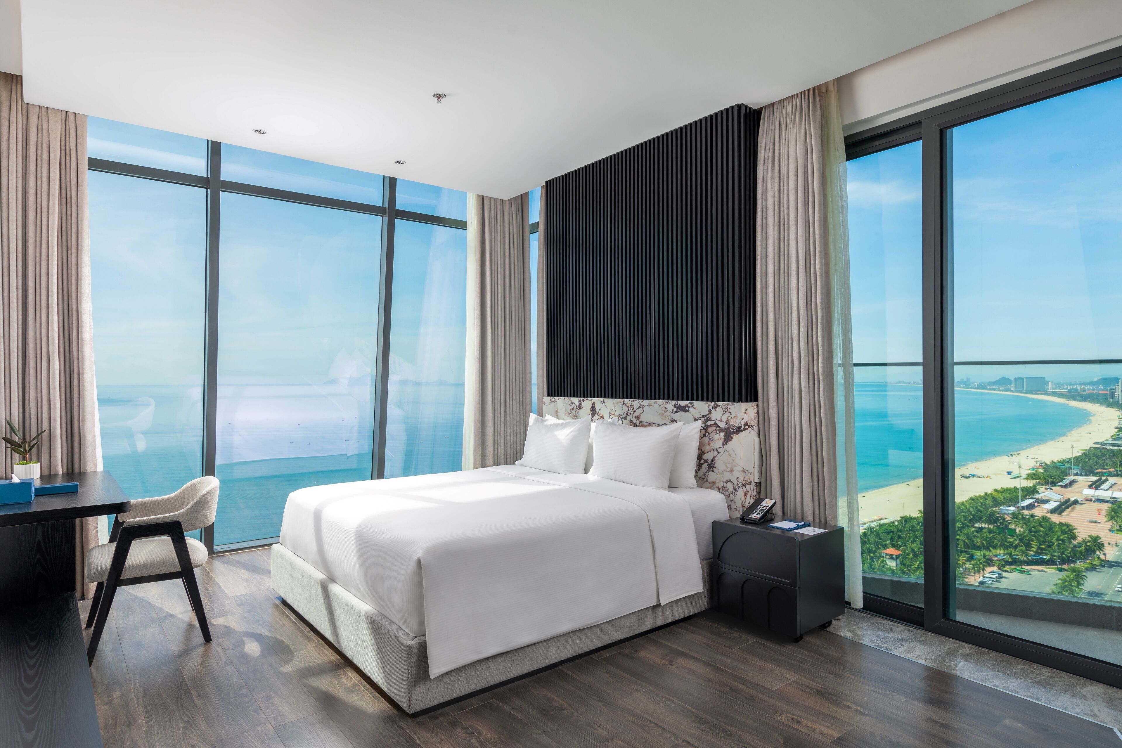 Habitació d'hotel moderna amb un llit gran, una taula de treball i una cadira. Disposa d'ampies finestres amb vista a la platja i a l'oceà.