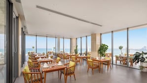 Uma ampla área de jantar com mesas e cadeiras de madeira, grandes janelas com vista para o mar e um design de teto moderno.