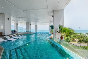 An indoor infinity pool with clear blue water, white tiled floor, and a glass balustrade. - Awaken Danang Hotel (Da Nang)