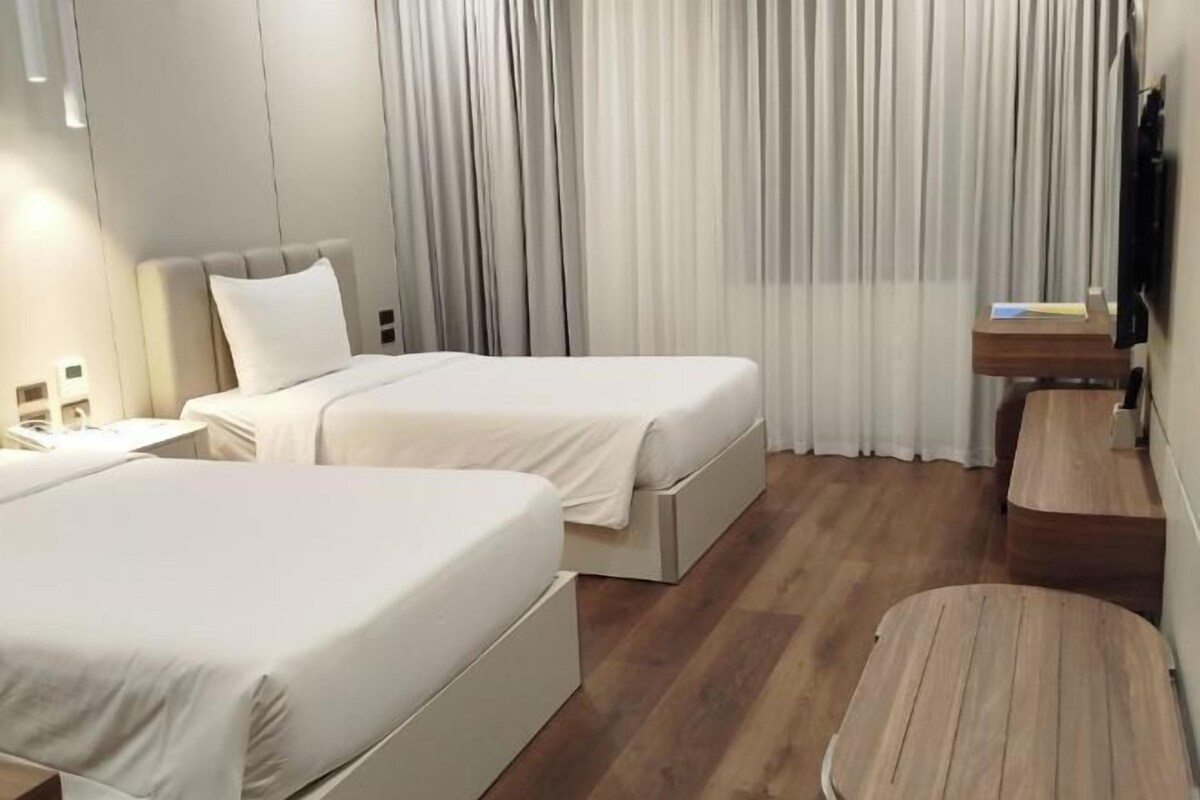 Een hotelkamer met twee eenpersoonsbedden, een houten vloer, een klein bureau en een televisie aan de muur.