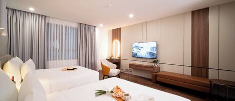 A hotel room with two beds, a TV, a desk, and a seating area.