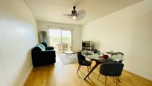 Een moderne woonkamer met een bank, een eettafel met stoelen en een plafondventilator.