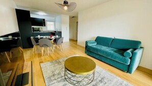 Een moderne woonkamer met een blauwgroene bank, een ronde salontafel, en een eethoek met stoelen en een tafel.
