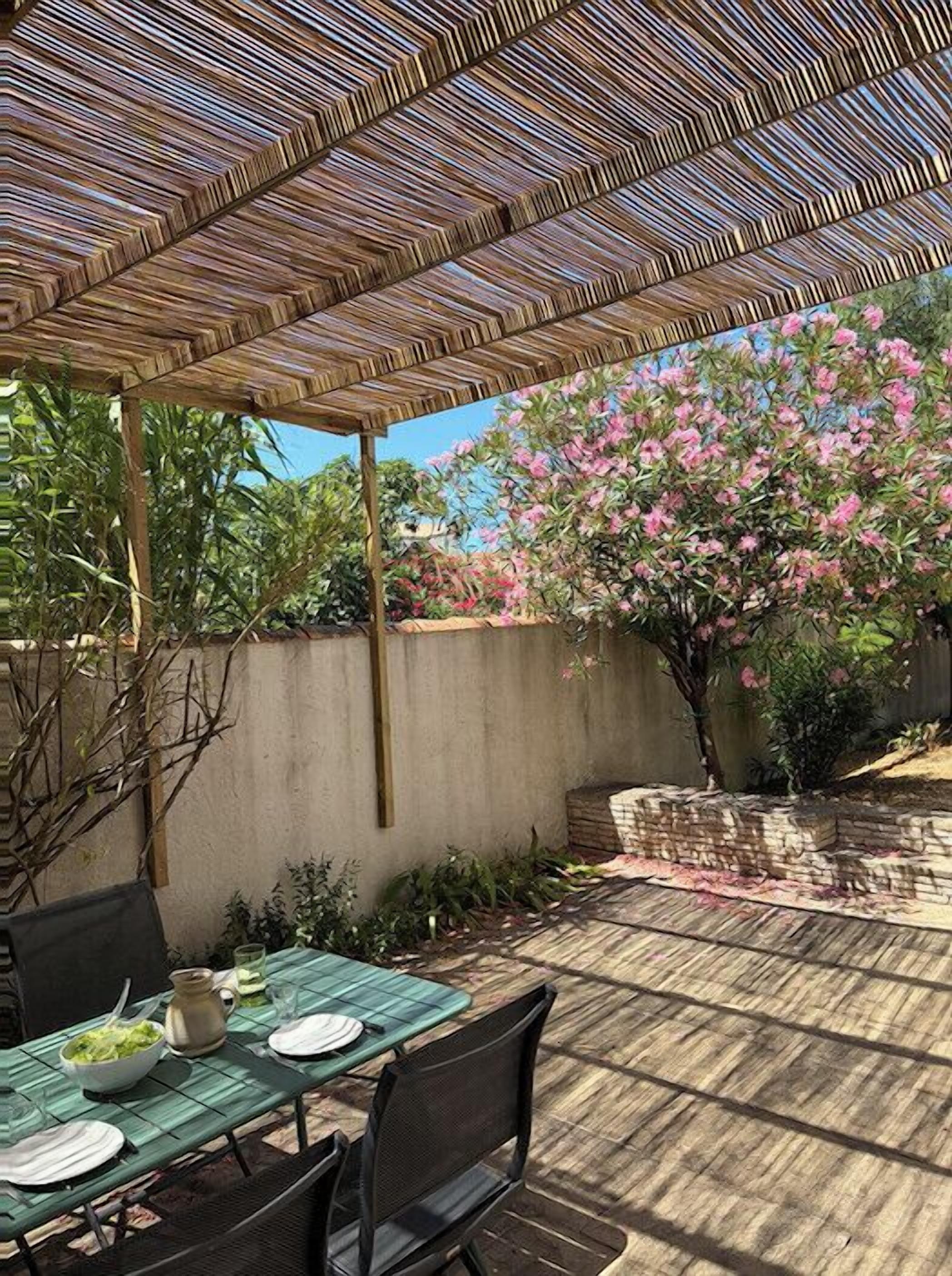 Un pati exterior amb una pèrgola de bambú, una taula preparada per dinar i un arbre amb flors al fons.