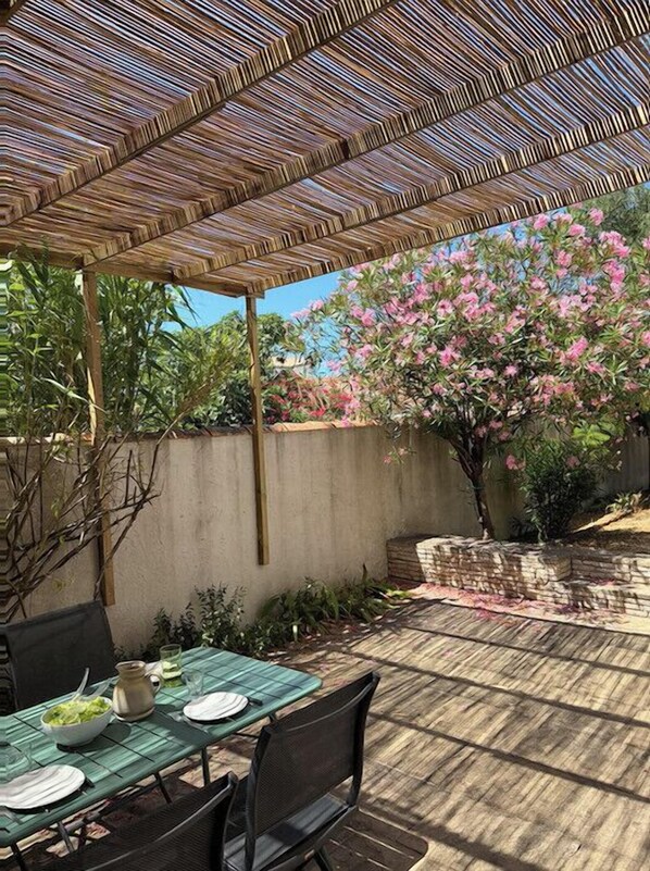 An outdoor patio with a bamboo pergola, a table set for dining, and a flowering tree in the background.