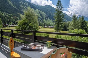 A table with a tray of cups and a mug, a bench, and a view of mountains and houses.
