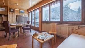 Una cabaña de madera acogedora con comedor, ventanas amplias y vistas a árboles nevados.