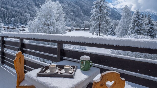 Un espacio al aire libre cubierto de nieve con una mesa dispuesta para dos, con vistas a un paisaje montañoso.
