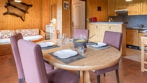 Un interior de madera con una mesa de comedor dispuesta para cuatro personas, un sofá y una zona de cocina.