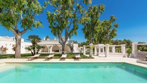 Ein Pool mit Liegestühlen, umgeben von Bäumen und einem weißen Gebäude mit Bögen.
