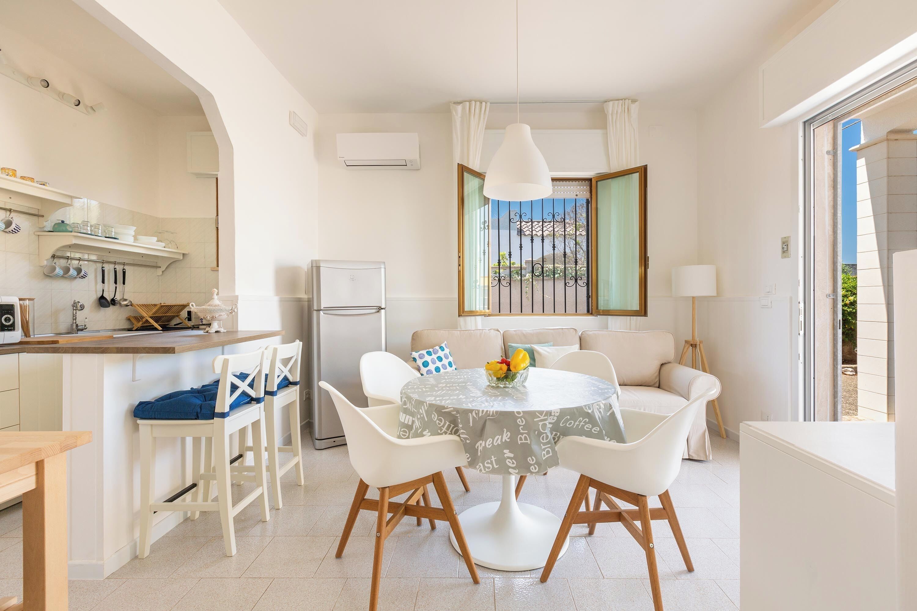 Una cocina moderna con armarios blancos, un refrigerador y un comedor con una mesa redonda y sillas blancas.