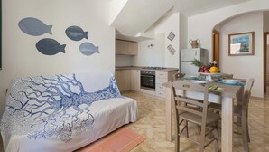 A cozy room with a bed, a dining table with chairs, a kitchen area, and a wall with fish decorations. - Affaccio Calipso - PT by BarbarHouse (Marittima)