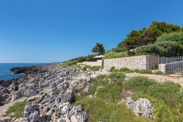 A coastal property with a stone wall, a wooden fence, and a view of the sea.