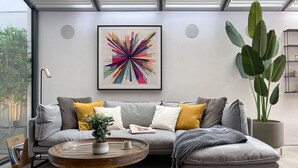 A modern living room with a grey sectional sofa, a round wooden coffee table, and a large green plant. - Luxury Urban Oasis: with Garden and Private Studio (London)
