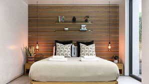 A modern bedroom with a suspended bed, wooden slats on the wall, bedside tables with plants, and a large window. - Luxury Urban Oasis: with Garden and Private Studio (London)