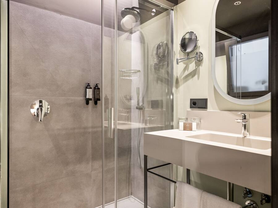 A modern bathroom with a glass-enclosed shower, a large mirror, and a white sink.
