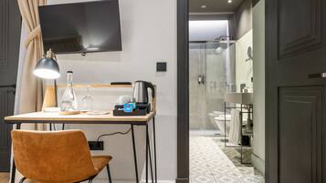 A modern hotel room with a desk, chair, television, and a shower area.