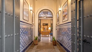 A hallway with blue and white patterned tiles, a wrought iron gate, and a bench. - Casa Alhaja by Shiadu (Seville)