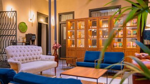 A modern living room with a white tufted sofa, blue armchairs, and a wooden coffee table. A wooden cabinet with glass doors displays various items. - Casa Alhaja by Shiadu (Seville)