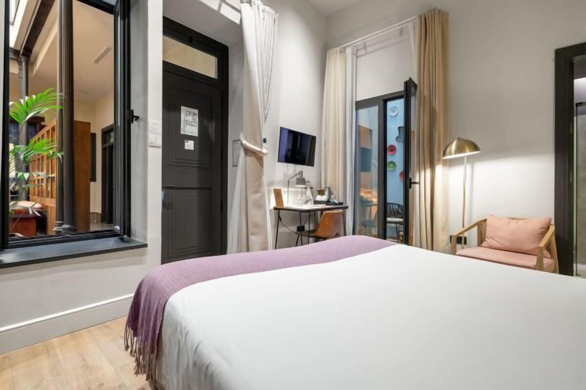 Une chambre d’hôtel avec un lit, un bureau, une chaise et une grande fenêtre.