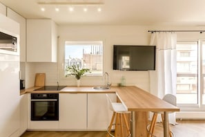 Una cocina moderna con armarios blancos, encimera de madera, horno empotrado, un lavamanos y una ventana con vista a la ciudad.