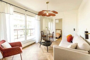 Una sala de estar moderna con un sofá, un sillón y una mesa de comedor con sillas. Hay un ventanal grande que proporciona luz natural y vistas al exterior.
