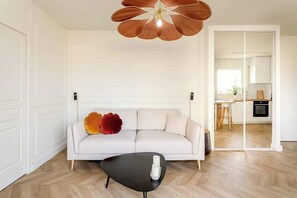 Una sala de estar moderna con un sofá blanco, una mesa de centro negra y una lámpara de techo con forma de flor.