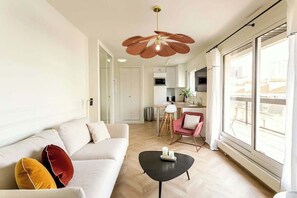 Uma sala de estar moderna com um sofá, uma mesa de centro e uma cozinha ao fundo.