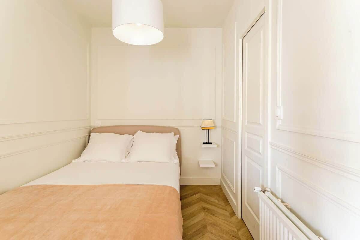 A bedroom with a bed, a nightstand, a lamp, and a radiator.
