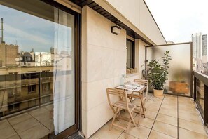 A balcony with a table and chairs, a potted plant, and a view of the cityscape.