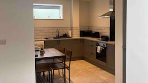 A modern kitchen with a dining area, featuring a window, built-in cabinets, and a range hood. - Remarkable 1-bed Studio in Downham Market (Downham Market)