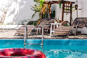 Un espace aménagé au bord de la piscine, avec des fauteuils de relaxation en osier, une table sur laquelle sont posées des bouteilles et une pergola.