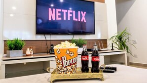 A modern living room with a flat-screen TV displaying the word "NETFLIX," a popcorn bucket, two Coca-Cola bottles, and a tray with remote controls. - Casa na Lapa com Piscina e Churrasqueira (São Paulo)
