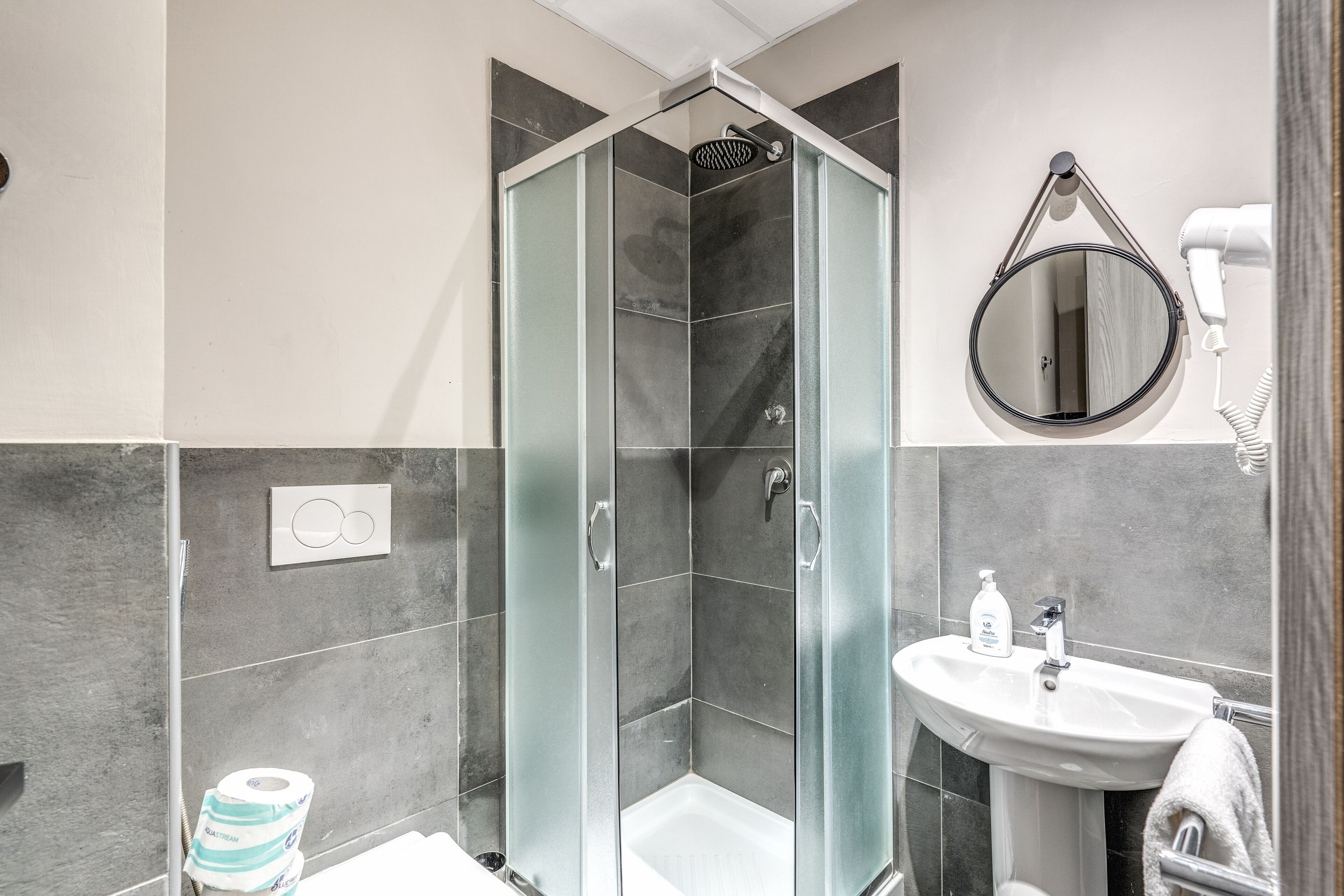 A modern bathroom with a glass-enclosed shower, a sink with a mirror, and a hairdryer on the wall.