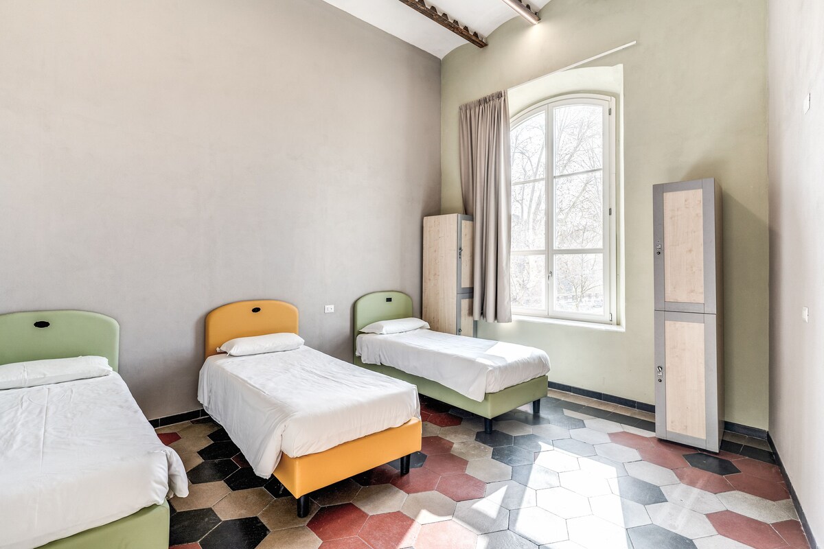 A room with three beds, a window with curtains, a cabinet, and a tiled floor.