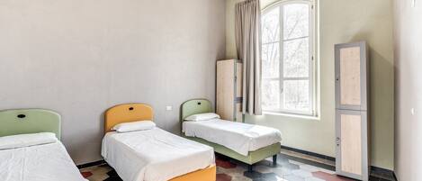A room with three beds, a window with curtains, a cabinet, and a tiled floor.