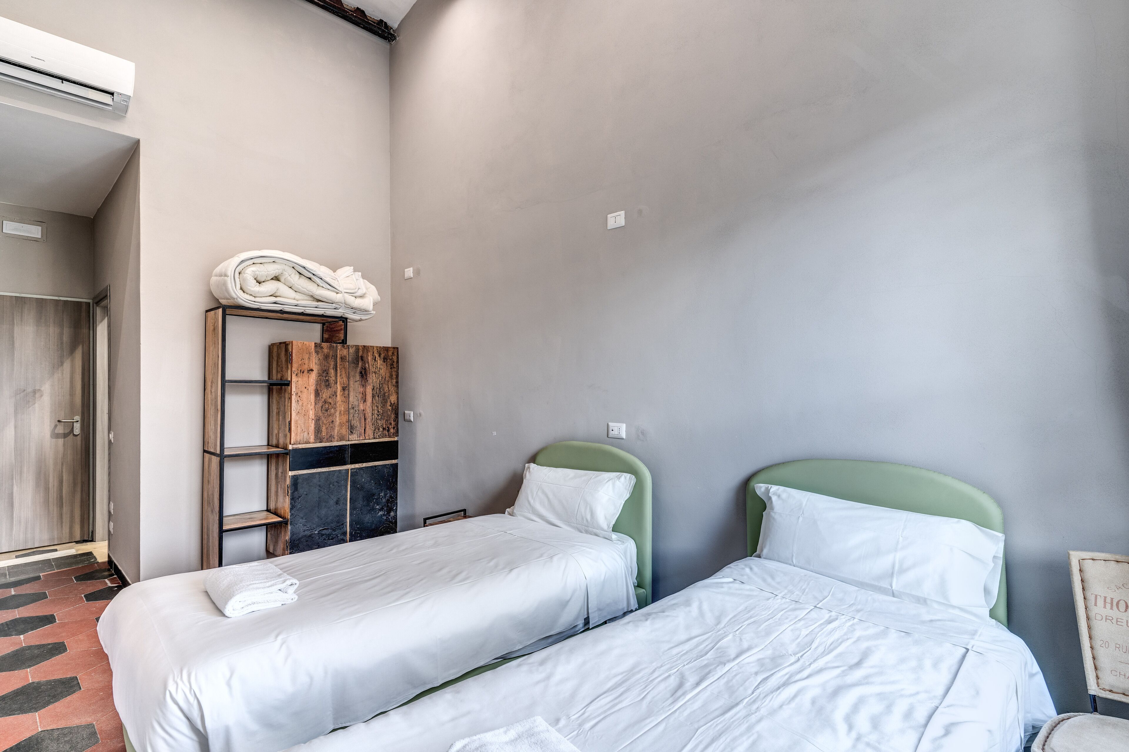 A room with two single beds, a wooden wardrobe, and a mirror.
