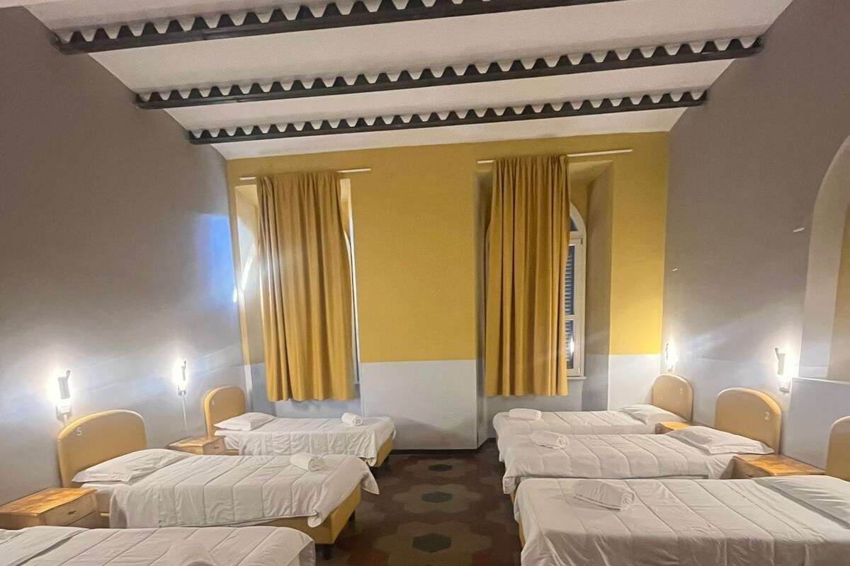 A hotel room with four beds, a patterned floor, and yellow curtains.