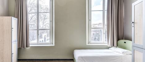 Una habitación con dos ventanas, una cama y un armario.