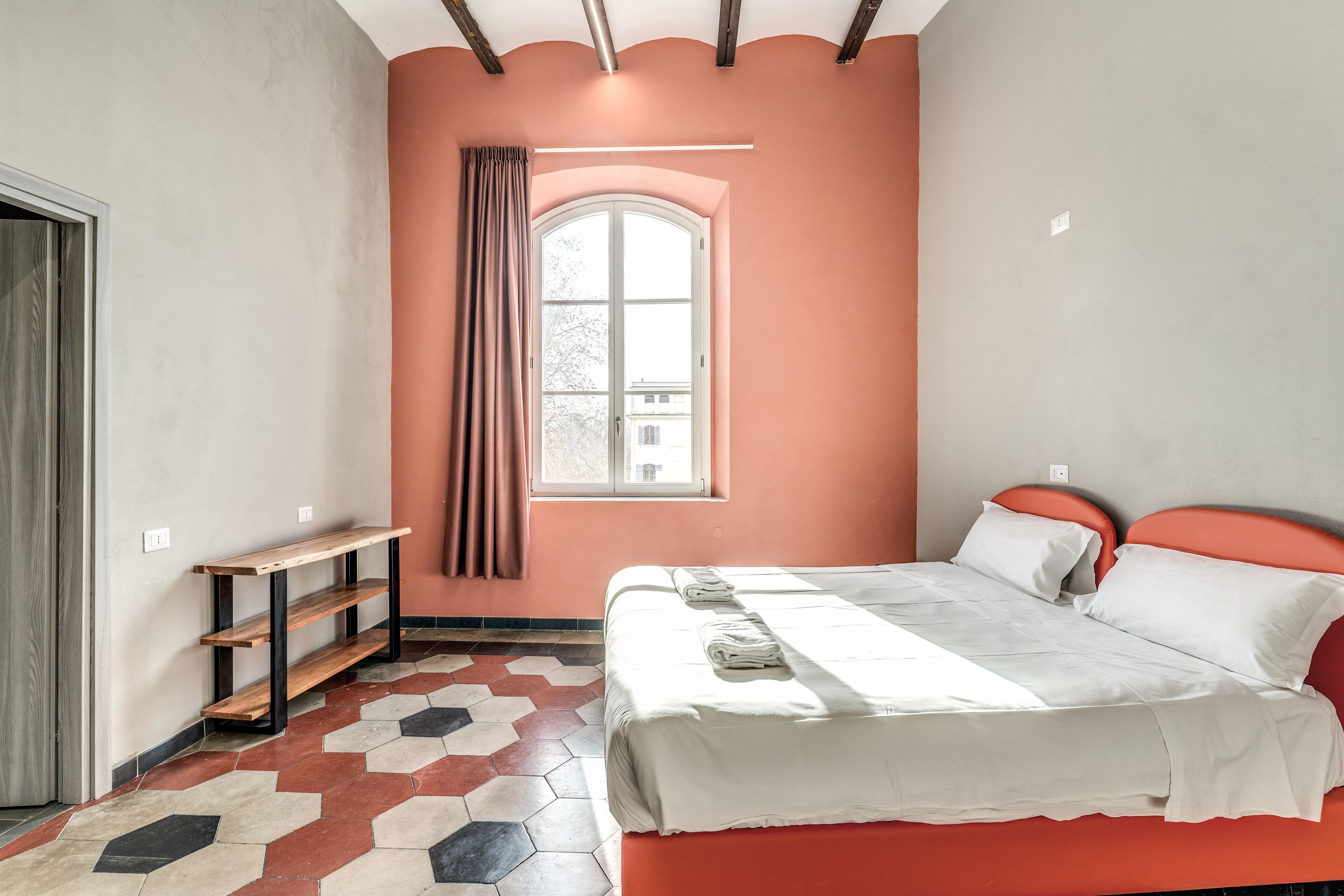 Une chambre à coucher avec un lit, une fenêtre donnant sur un beau paysage, un banc et un sol orné de motifs géométriques.