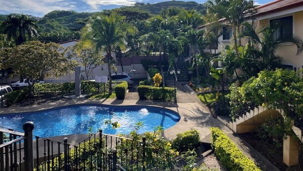 A swimming pool surrounded by lush greenery and a hilly landscape in the background. - Lovely Condo In Playa del Coco! (Coco)
