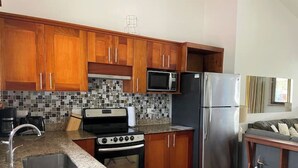 A kitchen with wooden cabinets, a stainless steel refrigerator, a microwave, a stove, and a tiled backsplash. - Lovely Condo In Playa del Coco! (Coco)