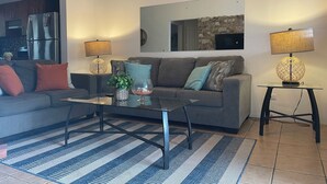 A living room with a sofa, coffee table, and lamps. There is a kitchen in the background. - Lovely Condo In Playa del Coco! (Coco)
