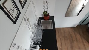 A kitchen with a black countertop, a sink, a toaster, and a potted plant. - Family A (Pakem)