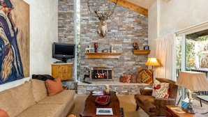 A cozy living room with a stone fireplace, a mounted deer head, and a television.